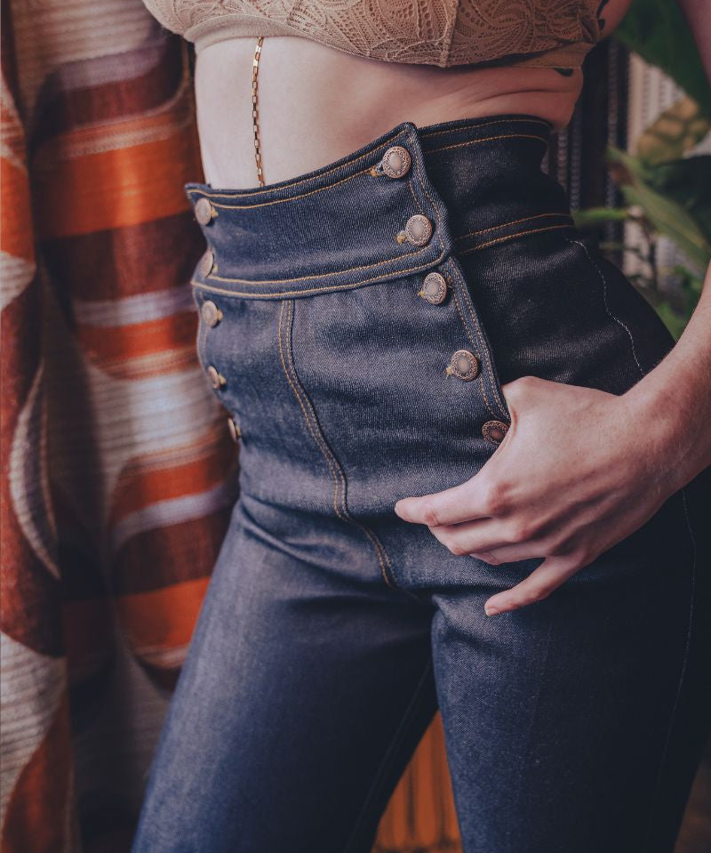 Person wearing a beige lace top and high-waisted blue jeans with a blurred background