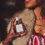 Woman holding a Soul Sister since 1969 perfume bottle with a fur coat and dark background