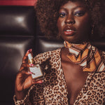 Woman in leopard print outfit holding a bottle of Soul Sister perfume with a gold scarf around her neck.