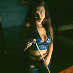 Woman holding a pool cue in a dimly lit room wearing sexy high waisted bell bottom jeans