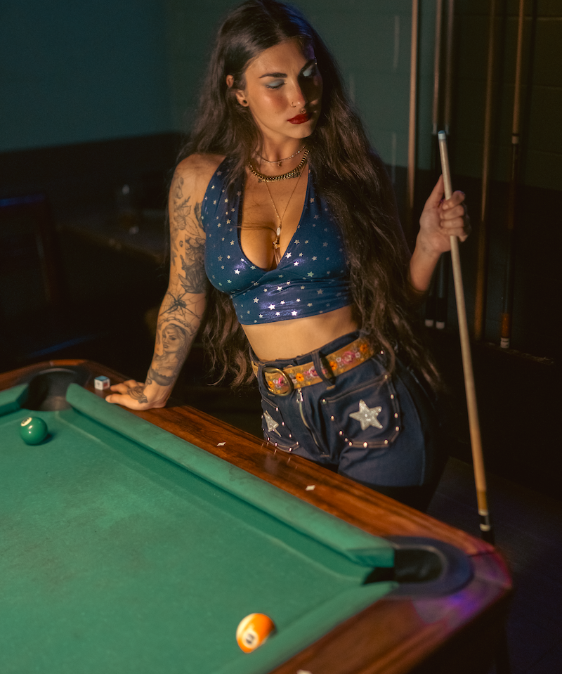 Woman playing pool wearing a groovy 70s retro inspired denim outfit  in a 1970s style dimly lit room
