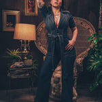 Model wearing a 70s inspired stretch denim jumpsuit with flared legs front zip closure and a plunging neckline styled for a bold retro look
