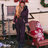 Woman in a purple snowsuit standing next to a wooden chair with a red and white blanket, in front of a trailer with Christmas decorations.