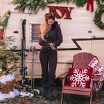 Person in winter clothing standing in front of a decorated trailer with 'JOY' and Christmas decorations.
