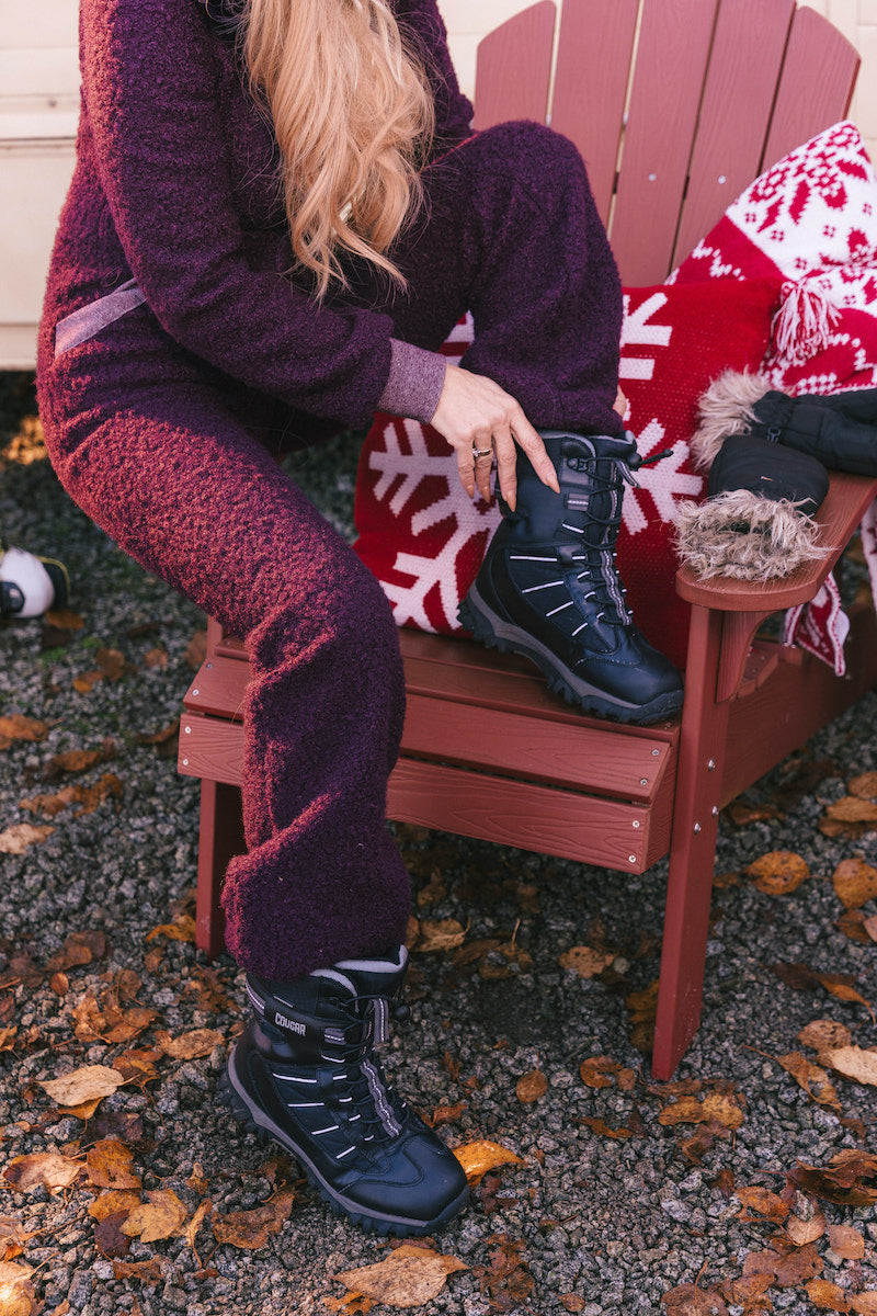 Person sitting on a red chair wearing dark purple pants and black boots, with a red and white patterned blanket.