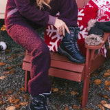 Person sitting on a red chair wearing dark purple pants and black boots, with a red and white patterned blanket.