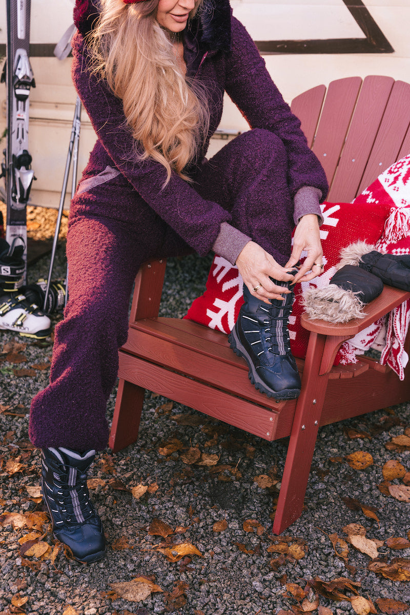Person in purple snowsuit sitting on a red Adirondack chair with skis and a blanket in the background.