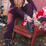 Person in purple snowsuit sitting on a red Adirondack chair with skis and a blanket in the background.