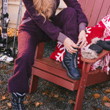 Person in purple snowsuit sitting on a red Adirondack chair with skis and a blanket in the background.