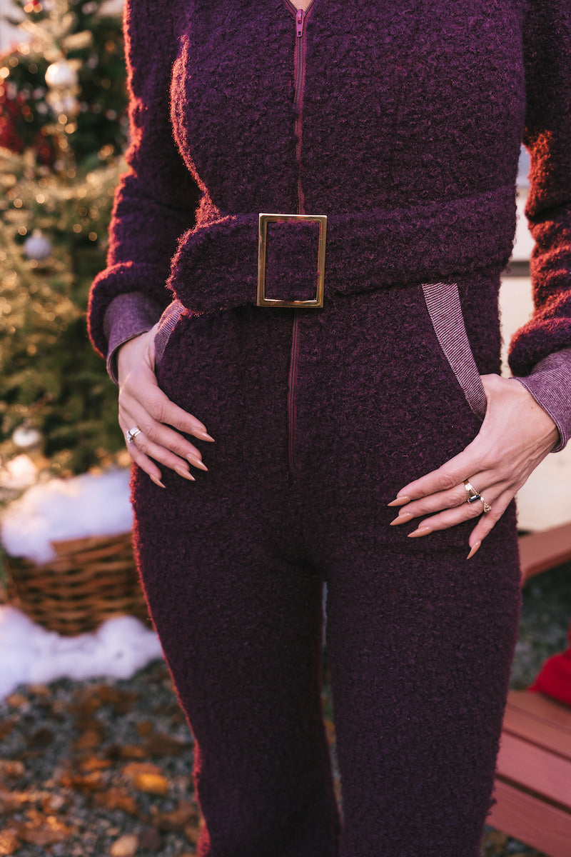 Person wearing a textured purple outfit with a belt in an outdoor setting.