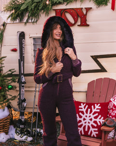Woman in a purple outfit standing in front of a Christmas-themed trailer with skis and a chair.
