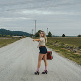 Woman hitchhiking on a rural road with a suitcase wearing Soul Sister since 1969.
