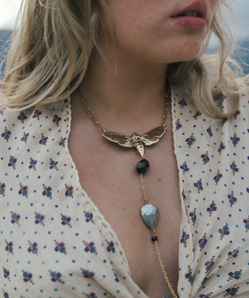 Close-up of a woman wearing a gold necklace with a butterfly pendant and black beads wearing Soul Sister since 1969..