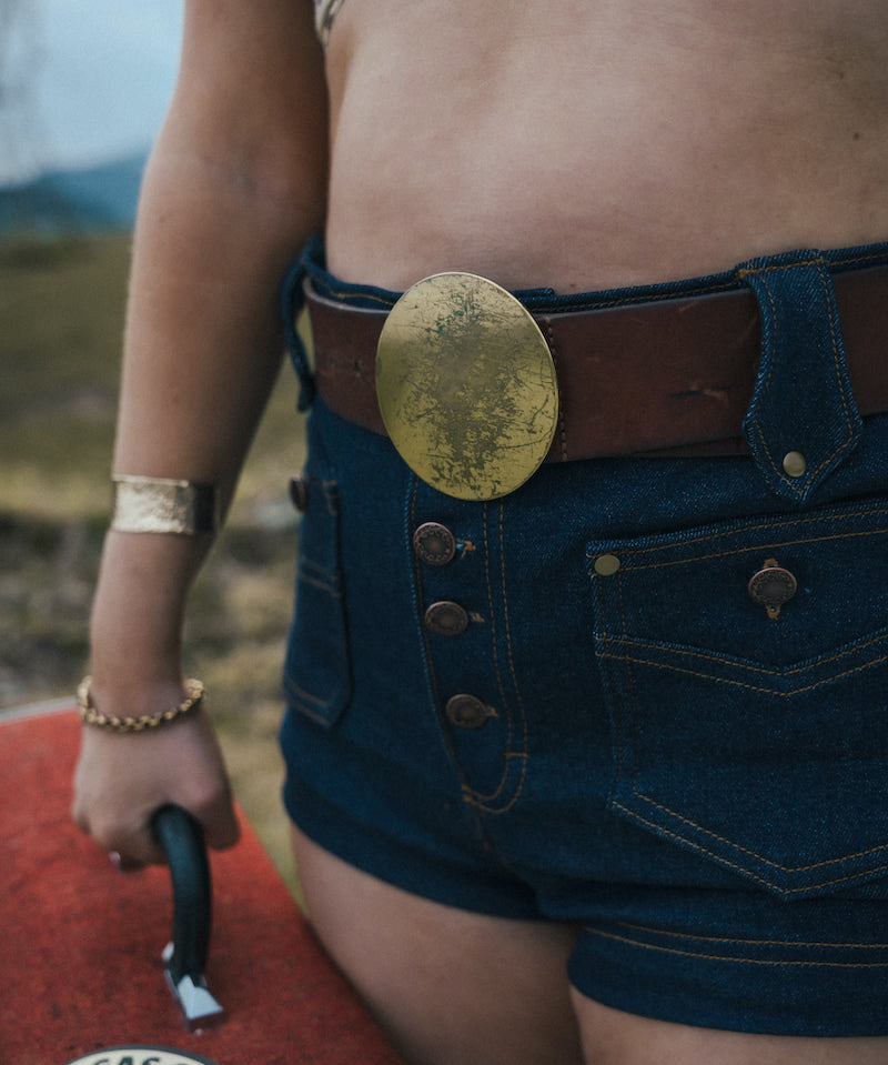 Person wearing a gold belt buckle and denim shorts with a blurred background wearing Soul Sister since 1969.
