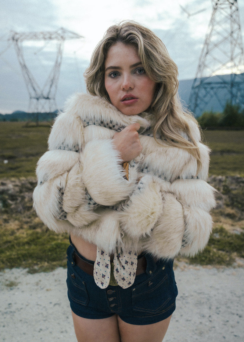 Woman wearing a fluffy white coat and gloves in an outdoor setting with power lines in the background wearing soul sister since 1969