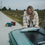 Woman in a fur coat looking at a map on a car hood by a road wearing soul sister since 1969