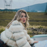 Woman in a white fur coat holding a map outdoors with mountains in the background wearing soul sister since 1969