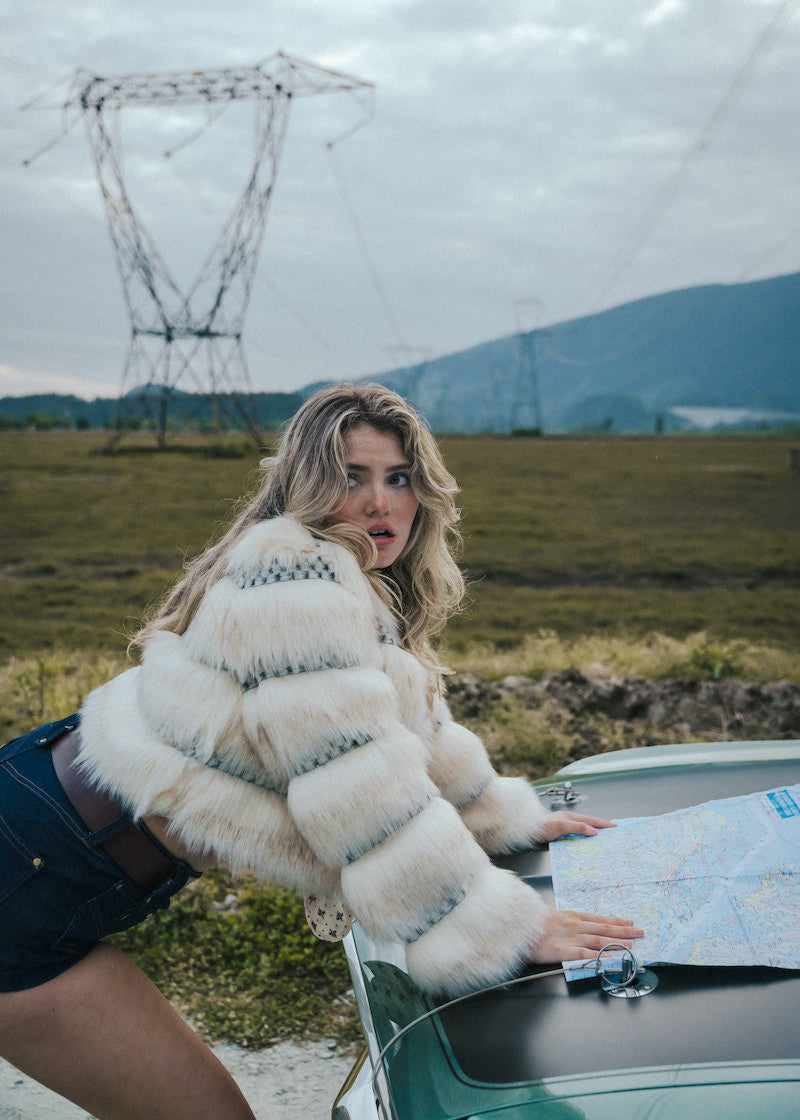 Woman in a fur coat looking at a map next to a car in a scenic outdoor setting wearing soul sister since 1969.