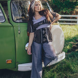 A woman standing beside a green van, wearing a black and white floral print tunic top with long sleeves, paired with gray pants.