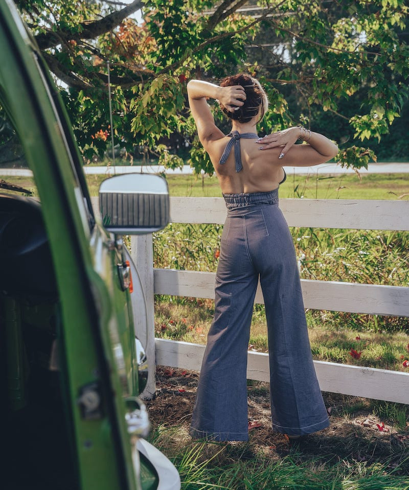 A person posing by a fence wearing high waisted bell bottoms and a sleeveless top.