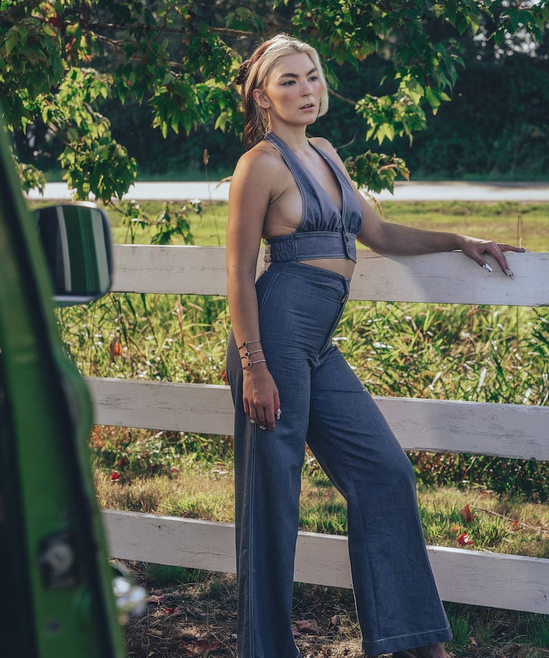 A person posing by a fence wearing high waisted bell bottoms and a sleeveless top.