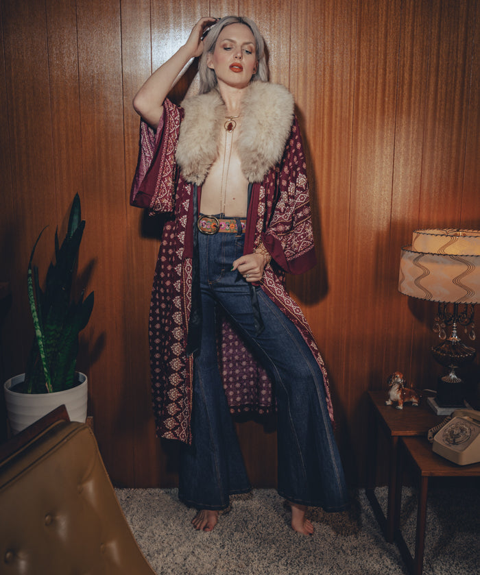 Bellbottom jeans are worn by a model in a retro styled 1970s living room

