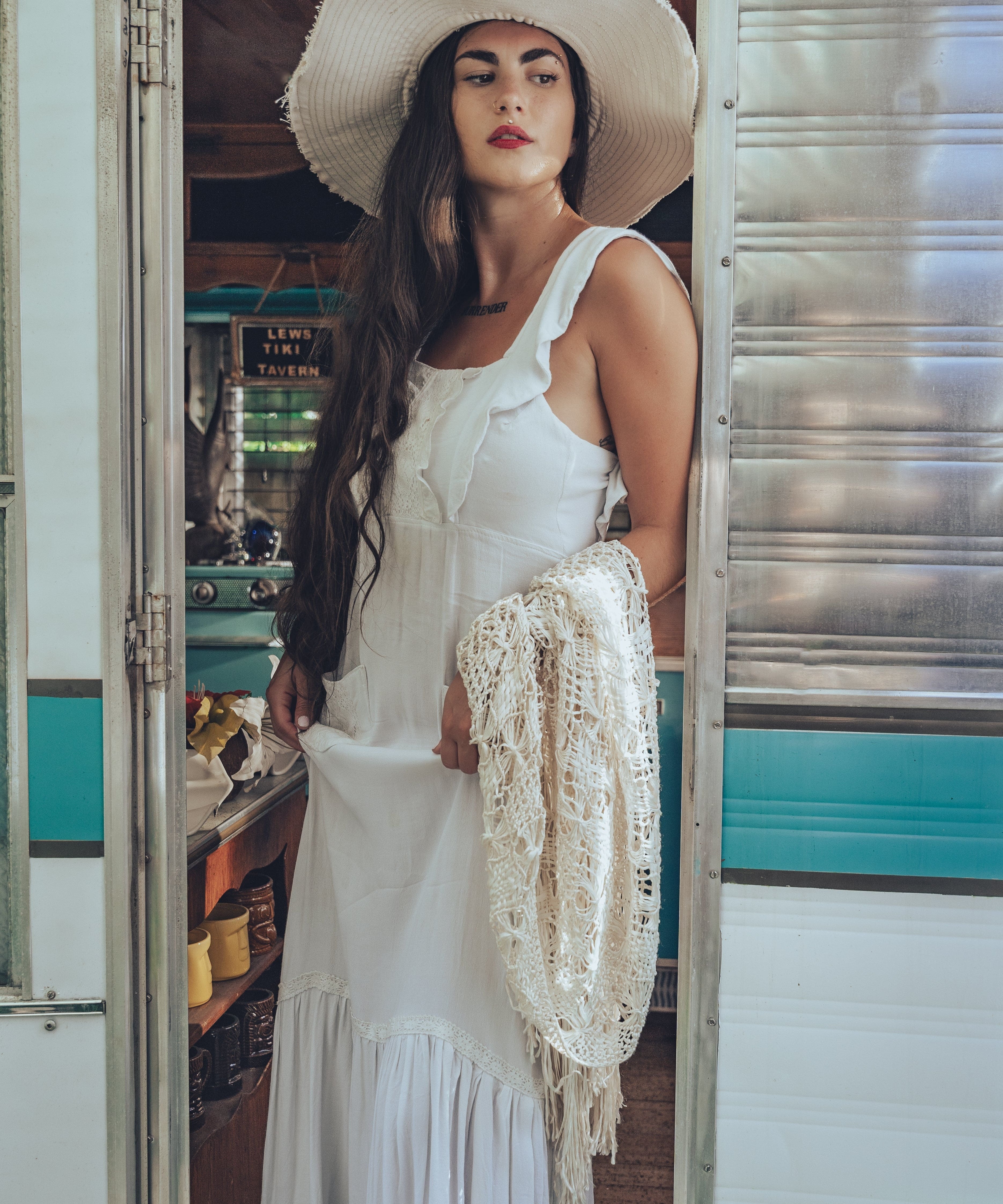 A beautiful woman with long dark hair wears a large white sunhat with a long bohemian white dress
