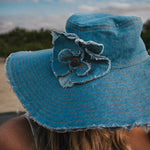 Blue denim sun hat with a flower detail against a blurred natural background Wearing Soul Sister since 1969