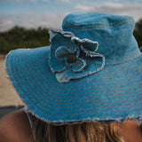Blue denim sun hat with a flower detail against a blurred natural background Wearing Soul Sister since 1969