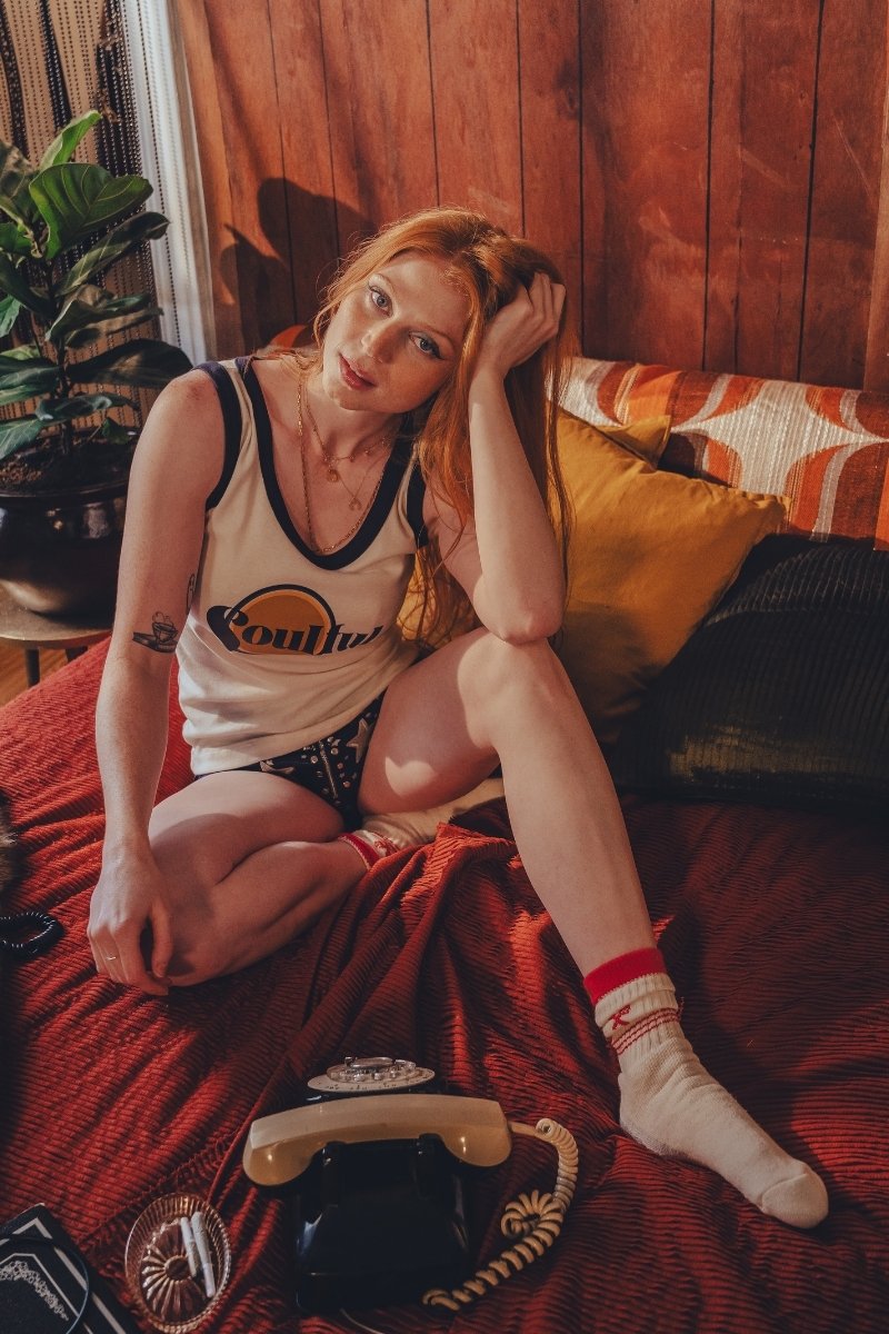Woman in a soulful log  jersey sitting on a couch with a retro phone and plant in the background