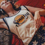 Person wearing headphones  in a 1970s style room and a tank top with a  soulful logo, lying on a red couch.