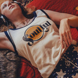 Person wearing headphones  in a 1970s style room and a tank top with a  soulful logo, lying on a red couch.