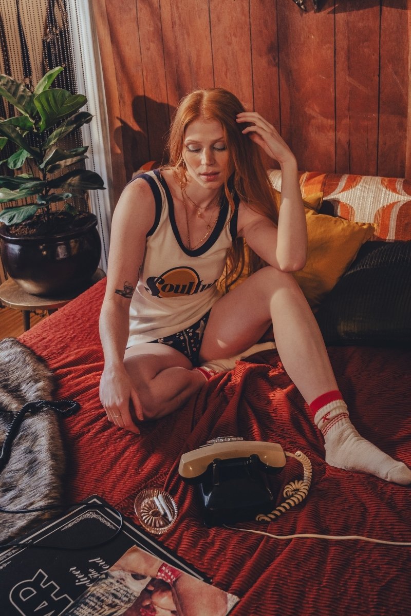 Woman sitting on a bed in a 1970s  inspired room with wooden walls and decor