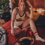 Woman sitting on a bed in a 1970s  inspired room with wooden walls and decor