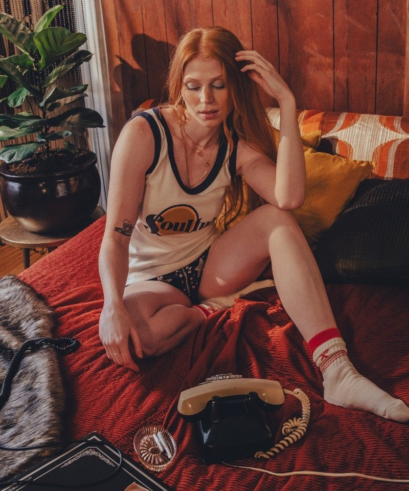 Woman sitting on a bed in a 1970s  inspired room with wooden walls and decor