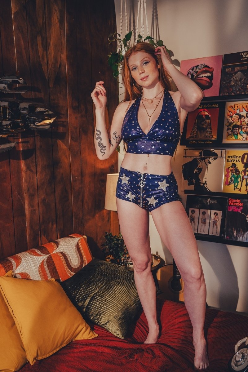 Woman in a blue star patterned 1970s diso ready outfit standing in a room with retro posters and decor.