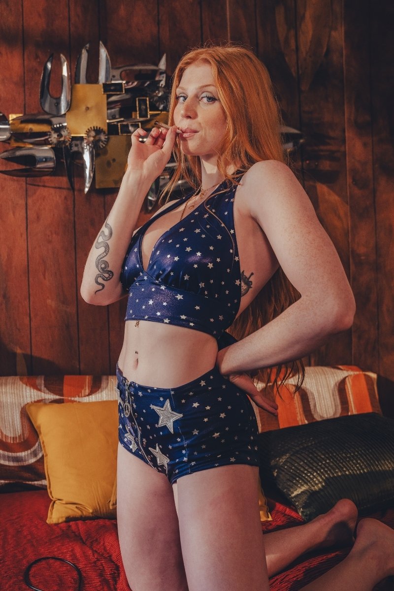 Woman in a blue star-patterned studio 54 inspired outfit standing in a room with 1970s wooden walls and art.
