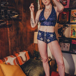 Woman in a blue and white star-patterned outfit standing in a room with a couch and decorative items.