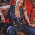 Woman in a stylish outfit sitting on a textured surface with a guitar in the background