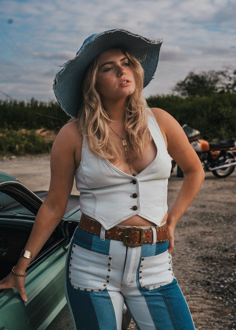 Woman in a white top and blue jeans standing next to a green car with a motorcycle in the background wearing Soul Sister since 1969..