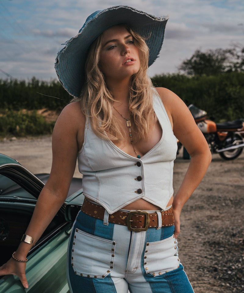 Woman in a white top and blue jeans standing next to a green car with a motorcycle in the background wearing Soul Sister since 1969..