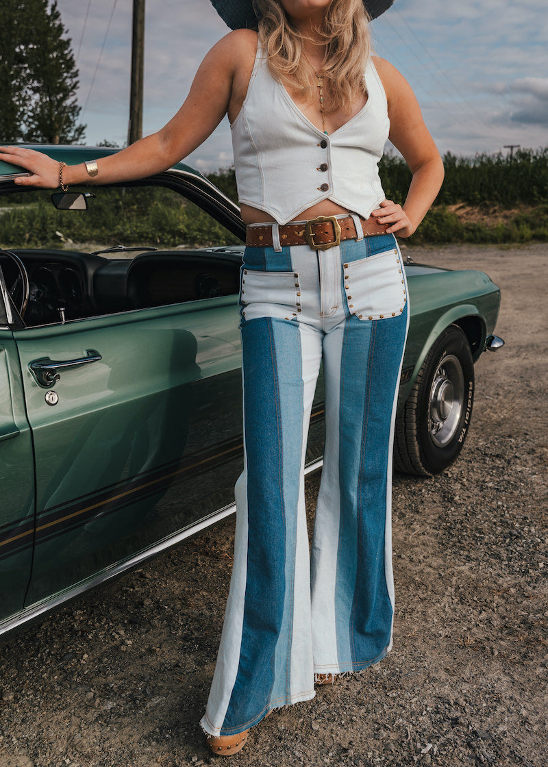 Woman in a white sleeveless top and blue bell-bottom pants standing next to a green classic car wearing Soul Sister since 1969..