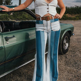 Woman in a white sleeveless top and blue bell-bottom pants standing next to a green classic car wearing Soul Sister since 1969..
