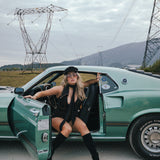 Woman leaning against a green car with power lines and mountains in the background wearing Soul Sister since 1969