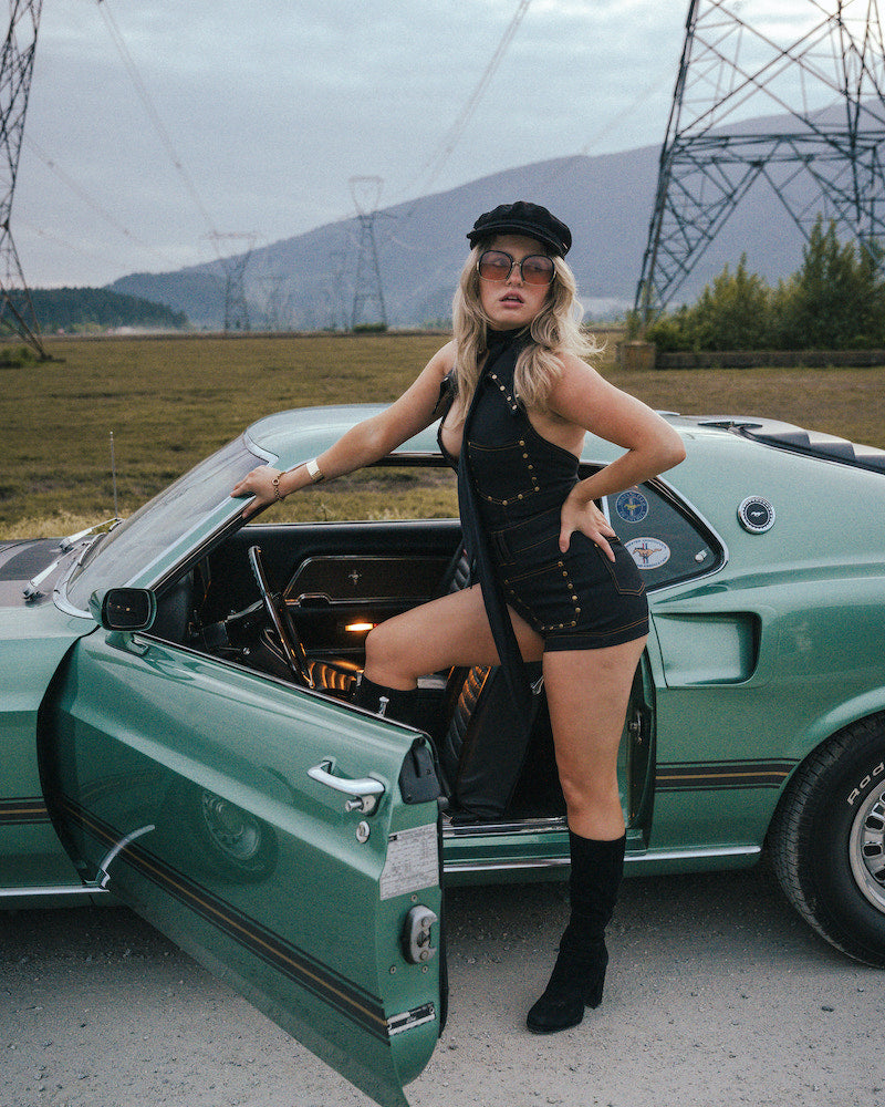Woman in a black outfit standing next to a green car with power lines and mountains in the background wearing Soul Sister since 1969