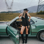 Woman in a black dress and boots standing next to a green car with power lines and mountains in the background wearing Soul Sister since 1969.