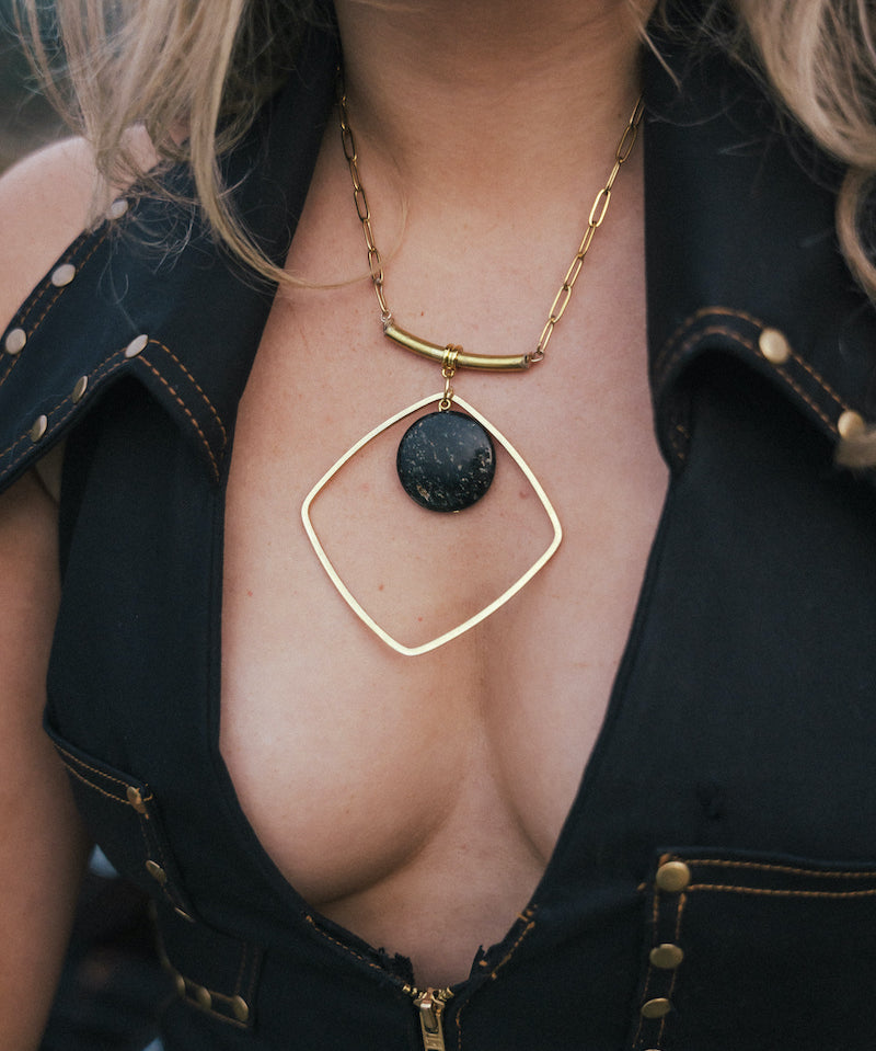 Person wearing a gold necklace with a black pendant, partially visible outfit