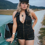 Woman in a black outfit standing next to a vintage car on a rural road wearing Soul Sister since 1969.