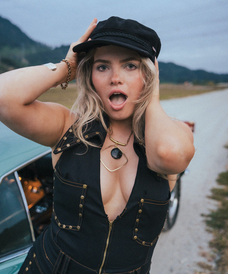 Woman in a black outfit and cap standing on a road with mountains in the background wearing Soul Sister since 1969