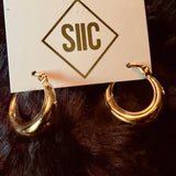 Gold hoop earrings on a card with 'SIIC' branding against a dark fur background